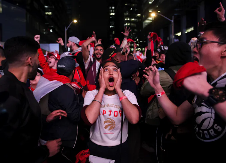Fans cheer and celebrate the Toronto Raptors victory outdoors at night.