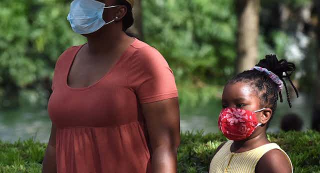A child and her mother wearing face masks as a preventive measure walk at Lake Eola Park on the day that Florida reported 12,180 new coronavirus cases.