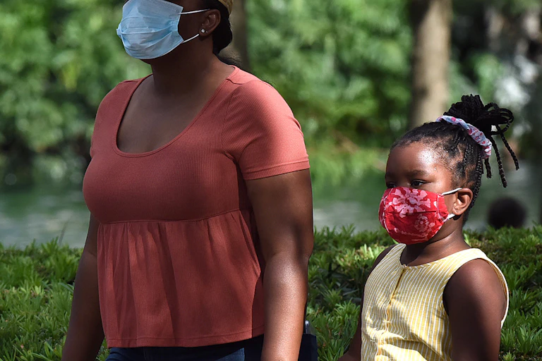 A child and her mother wearing face masks as a preventive measure walk at Lake Eola Park on the day that Florida reported 12,180 new coronavirus cases.
