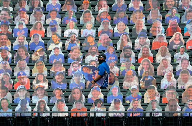 An employee of the New York Mets baseball team carries a cardboard cutout of a fan that will be placed in the empty stands.