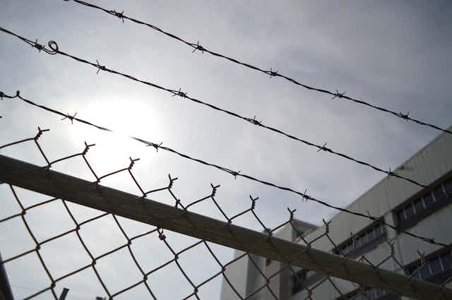 A prison chain-link fence topped by barbed wire