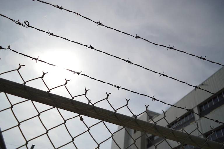 A prison chain-link fence topped by barbed wire