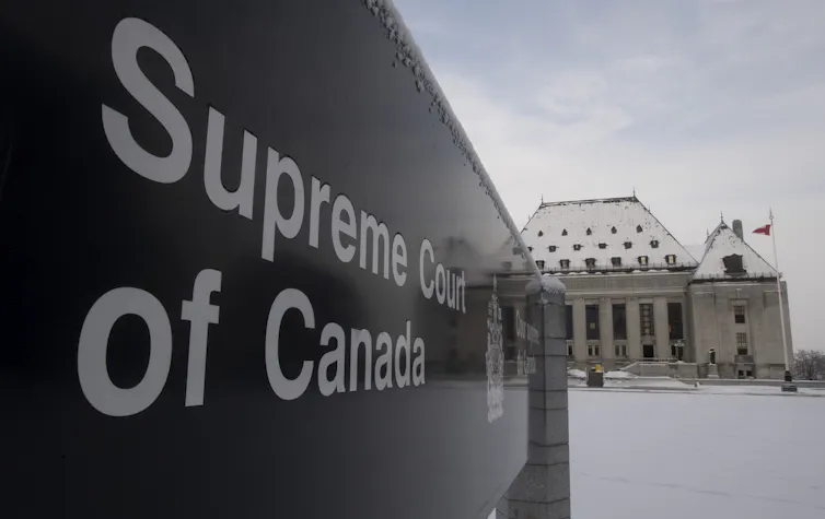 A sign reads Supreme Court of Canada with the Supreme Court buildings in the background with snow on the ground.