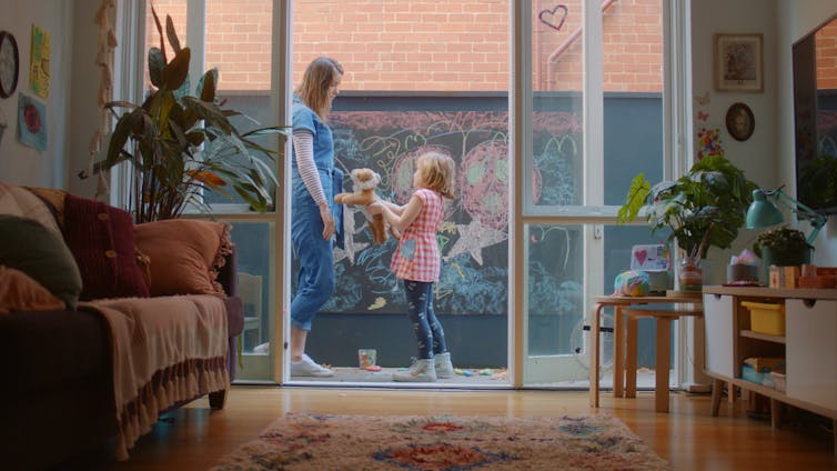 View from an apartment to a balcony, where a mum stands with her daughter.