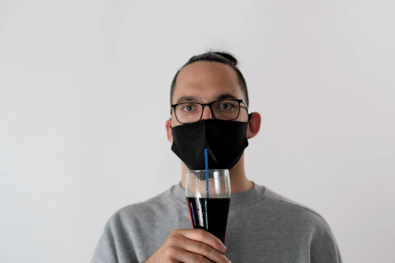 Un hombre con mascarilla bebe de un vaso con una pajita