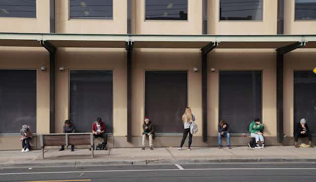 People sitting in a socially-distanced line outside a building