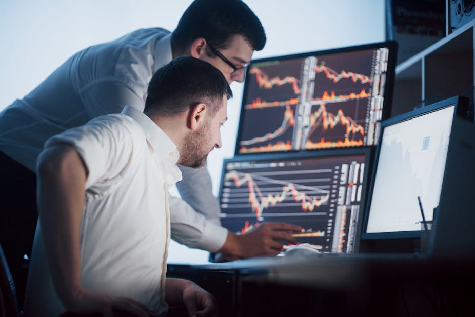 Two stockbrokers look at data on screens.