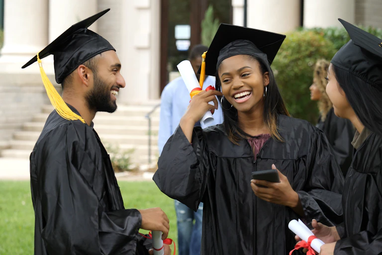 Three graduate students smile happily on graduation day on campus.