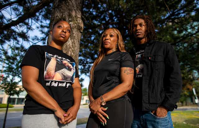 Three Black people, a young woman, her mother and brother, stand in front of a tree.