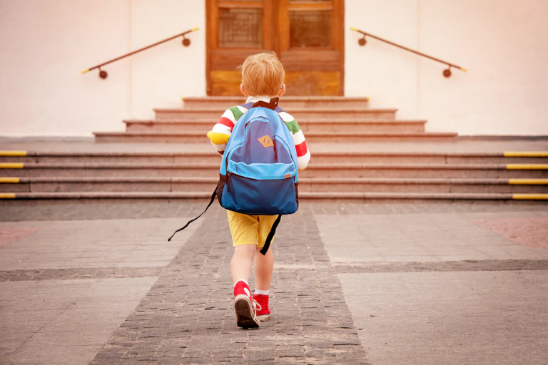 Niño de espaldas con mochila a la puerta de un colegio.