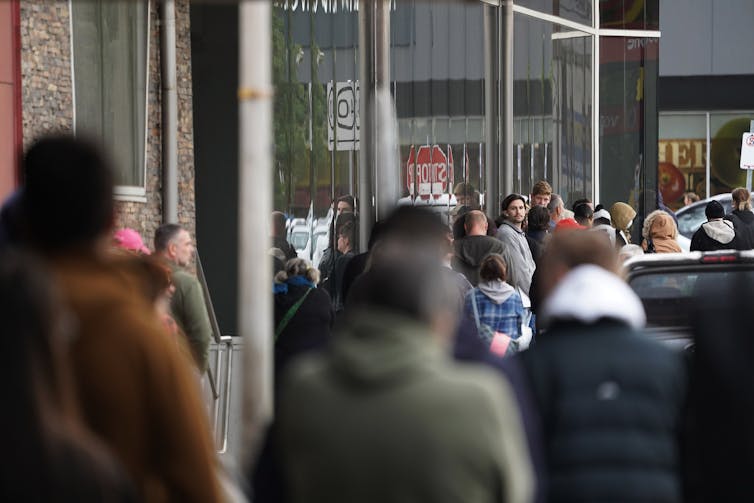 Line of people with their backs to camera, standing next two an office block