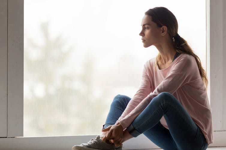 Sad woman sitting on floor staring out window