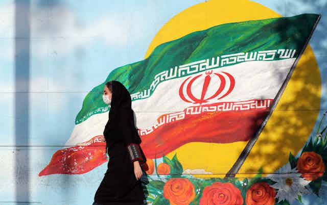 Women in Iran walks past painting of Iranian flag