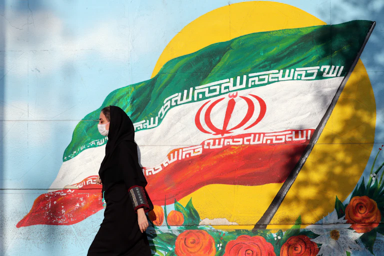 Women in Iran walks past painting of Iranian flag