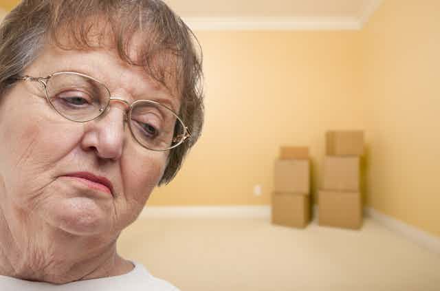 Older woman looks sad as she prepares to move house with packing boxes in an empty room 