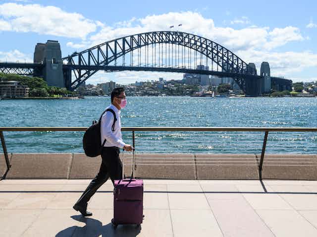 A man wearing a surgical mask walks in front of the Sydney Harbour Bridge.