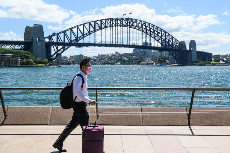 A man wearing a surgical mask walks in front of the Sydney Harbour Bridge.