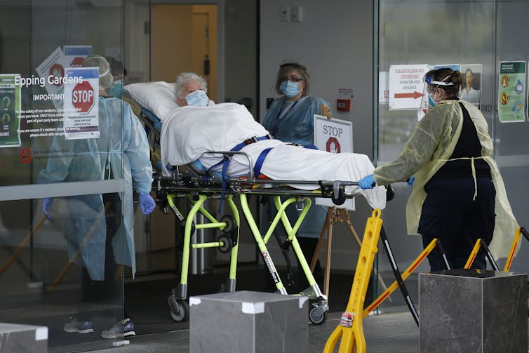 Emergency workers wheel an elderly resident on a stretcher out of an aged-care home