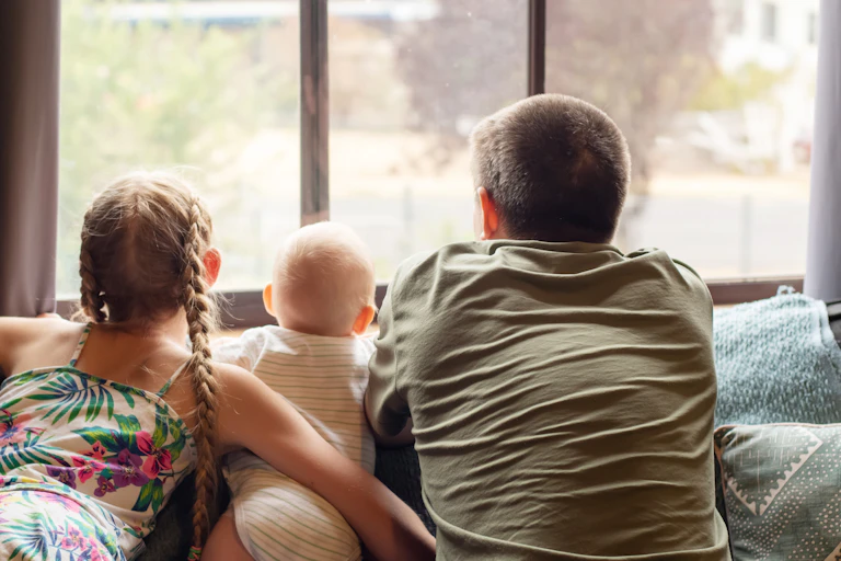 A father and his two children sitting inside, looking out of the window.