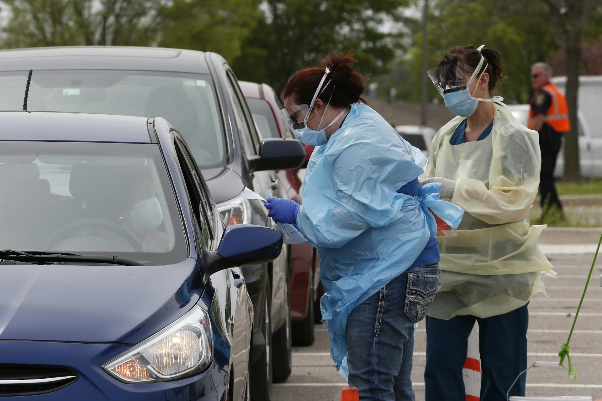 Two health care works standing outside preparing to perform a swab test at a drive-through testing station.