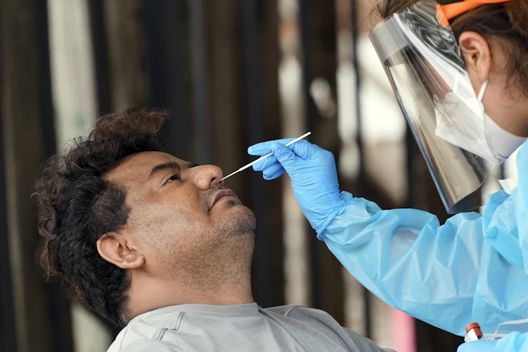 A female medical worker with face shield and gloves inserting a swab into a mans nose to perform a COVID-19 test.