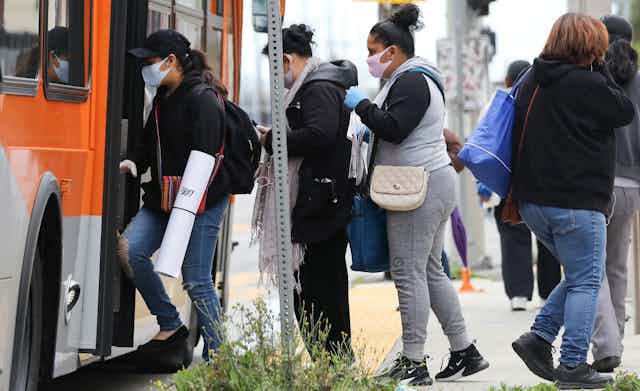 People wearing face masks board a bus in South Los Angeles in April 2020.