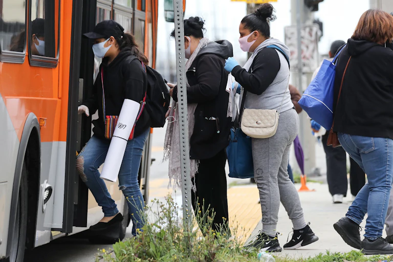 People wearing face masks board a bus in South Los Angeles in April 2020.