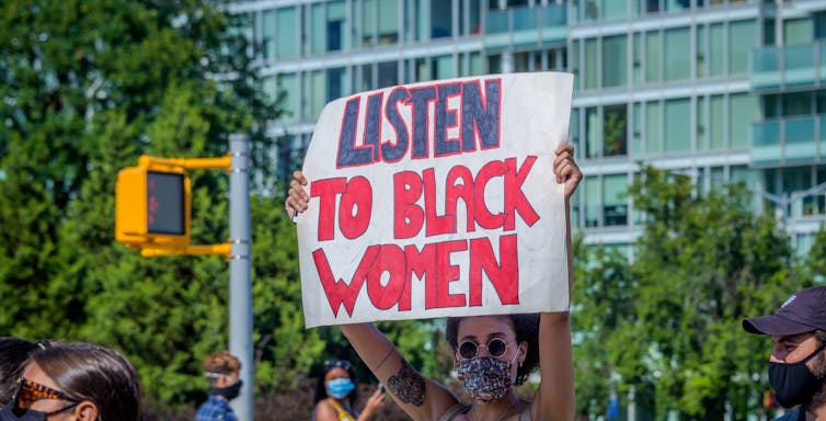 A participant holds a 'Listen to Black Women' sign at a protest in Fort Greene Park in Brooklyn, NY.