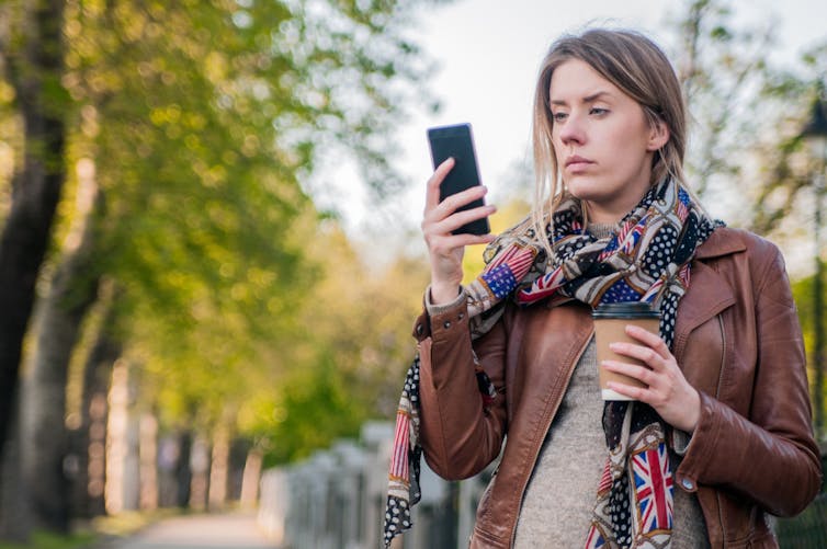 Young woman looking concerned, while looking at her phone.