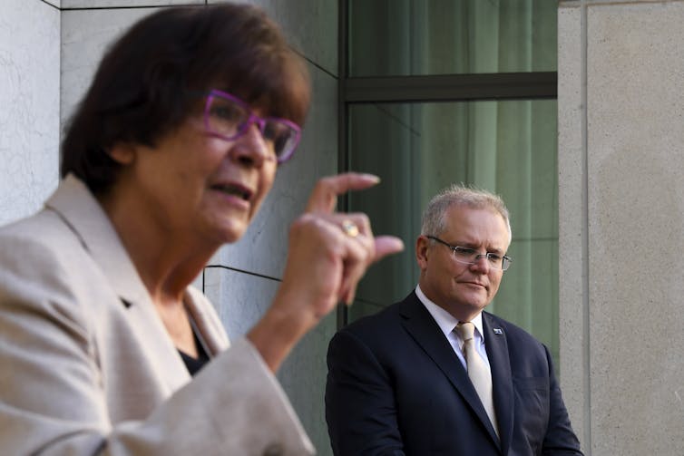 Pat Turner measuring an amount with her hand, with Scott Morrison in the background.