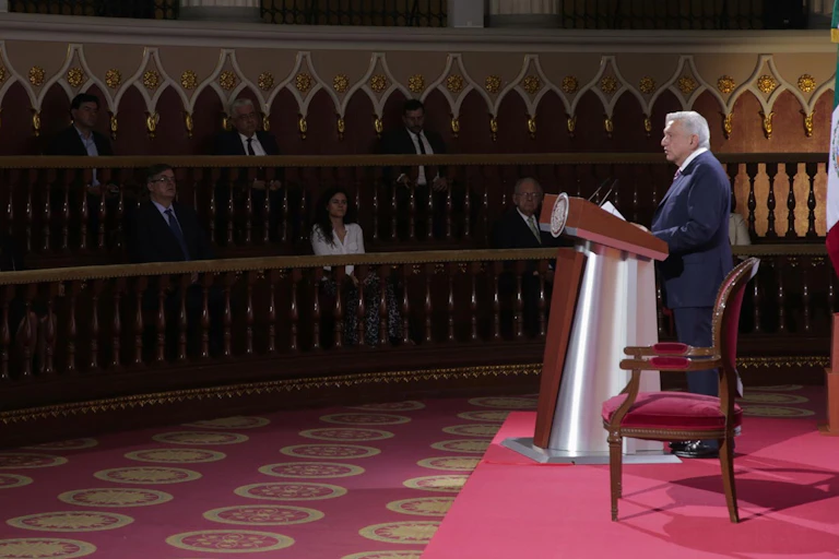 El presidente de México, Andrés Manuel López Obrador. lee un discurso ante una audiencia que escucha entre sombras.