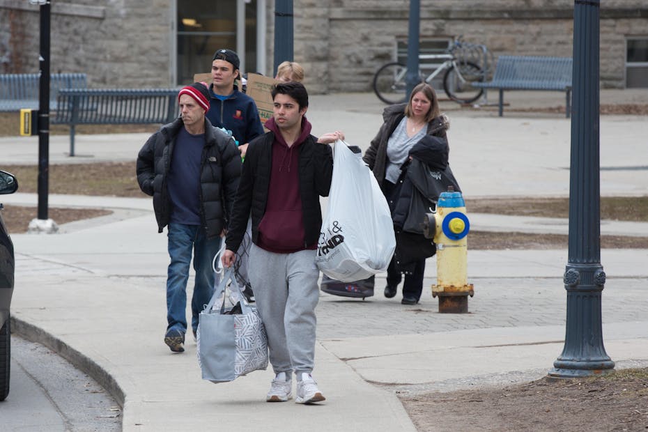 Students carrying bags and suitcases walk in a group on a grey sidewalk.