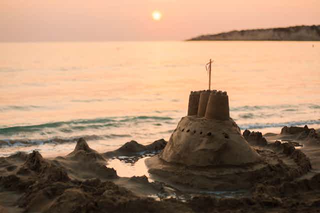 A sand castle is overtaken by the tide at dusk.