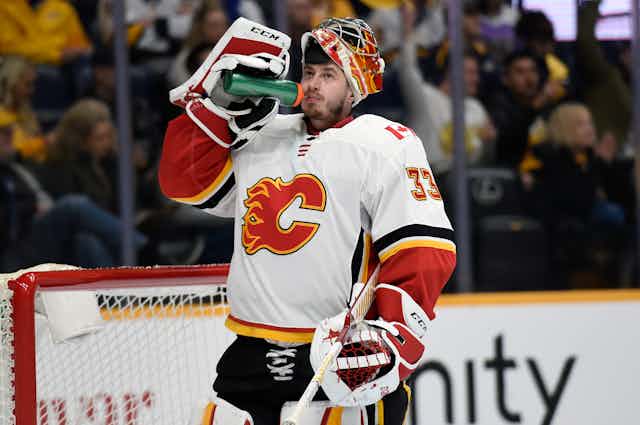 A Calgary Flames hockey player in a jersey with a flaming C drinks water.