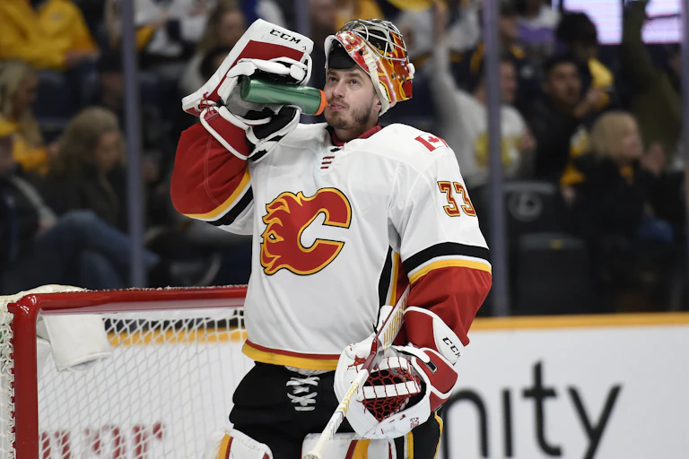 A Calgary Flames hockey player in a jersey with a flaming C drinks water.