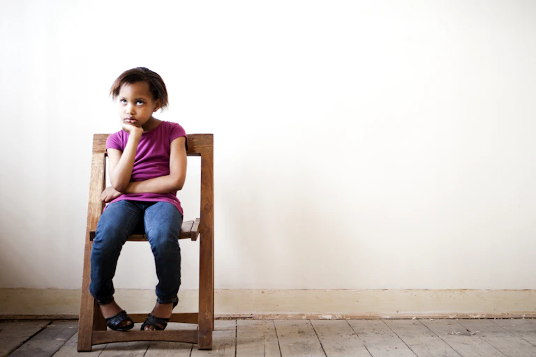 Bored child sitting in chair looking out into the distance.