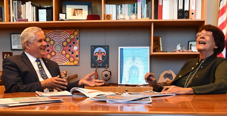 Two Indigenous political leaders chat and laugh at meeting table