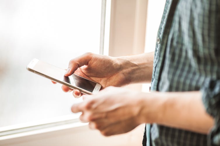 Man scrolling on smartphone next to window.