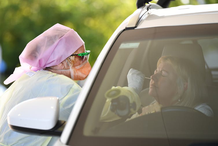 Woman in car receives a nasal swab from a health worker