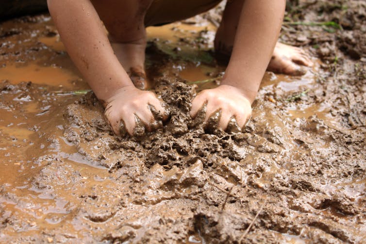 A child's hands playing with mud in a puddle.