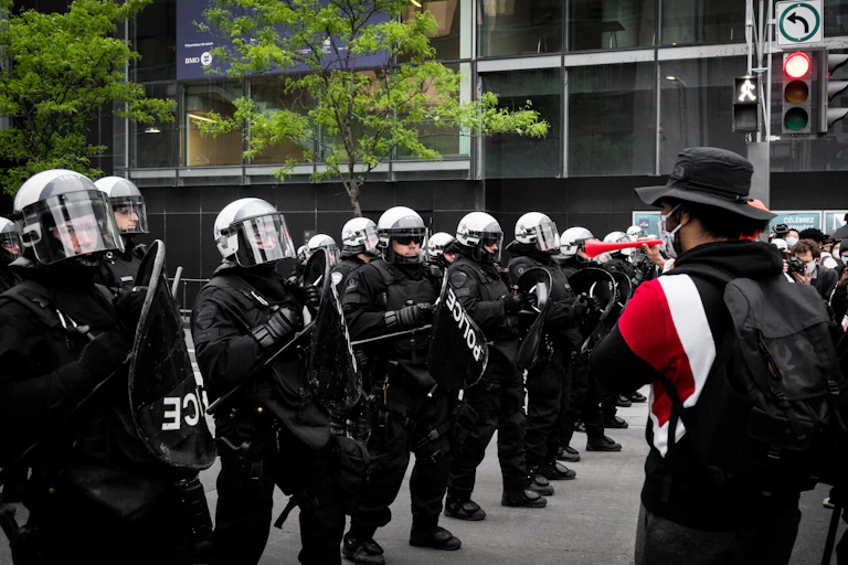 A row of police in riot gear face off against protestors.