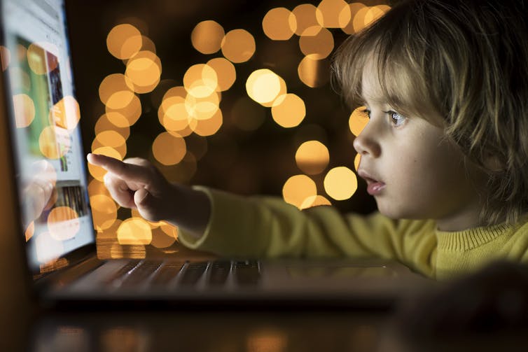 Toddler looks at a laptop in the dark.