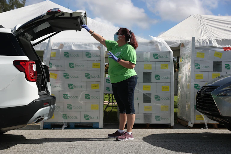 Loren Mennes place food in the back of a vehicle at a drive-thru food distribution site set up at the First Church of the Brethren on July 24 in Miami, Florida.