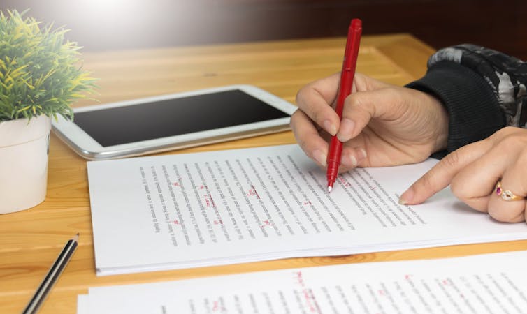 Hand holding red pen to edit paper.