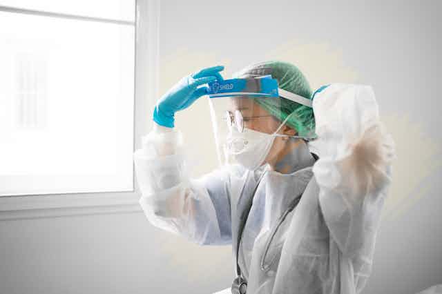 Female health-care worker wearing PPE adjusts face shield.