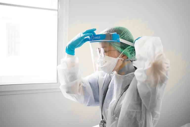 Female health-care worker wearing PPE adjusts face shield.
