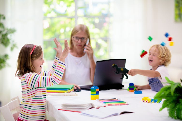 Mother working on computer with children playing around her.