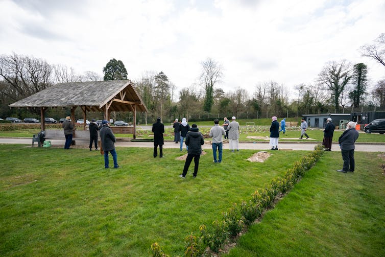 People stand at a distance for a funeral service.