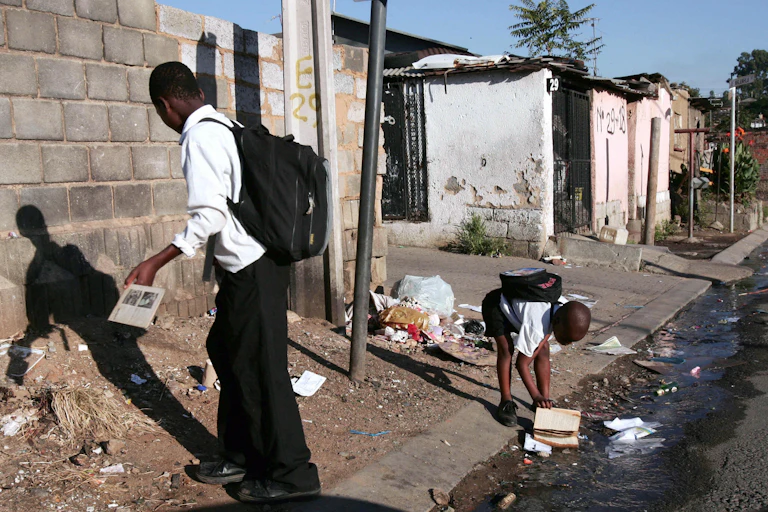 Schoolboys on the street, where a blocked drain is causing dirty water to leak out