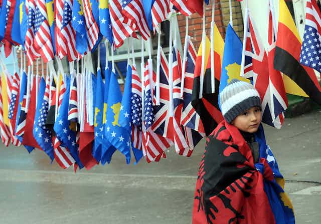 A boy wrapped in the Albanian and Kosovan flags in front of other national flags.